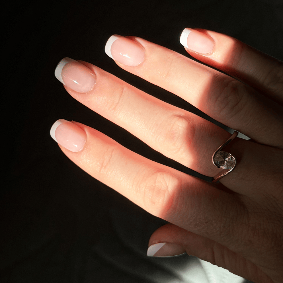 A hand with a ring and french tip press son nails on a dark background