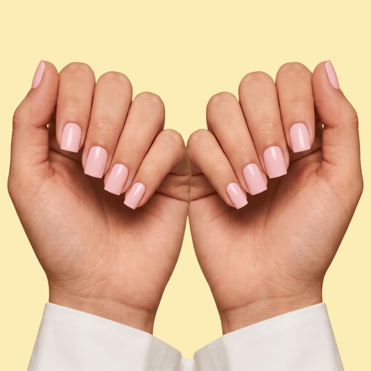 A close-up of two hands with neatly manicured nails painted in a soft light pink, shown against a pale yellow background with a white shirt cuff visible at the bottom.