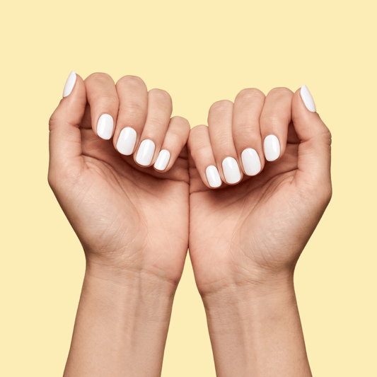 A pair of hands with neatly manicured, glossy white oval-shaped nails, posed against a solid pale yellow background.