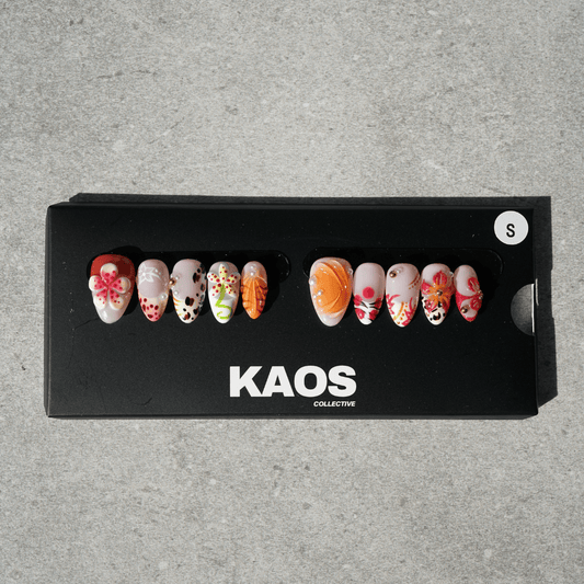 Set of decorative false nails in a black 'KAOS Collective' box on a gray background