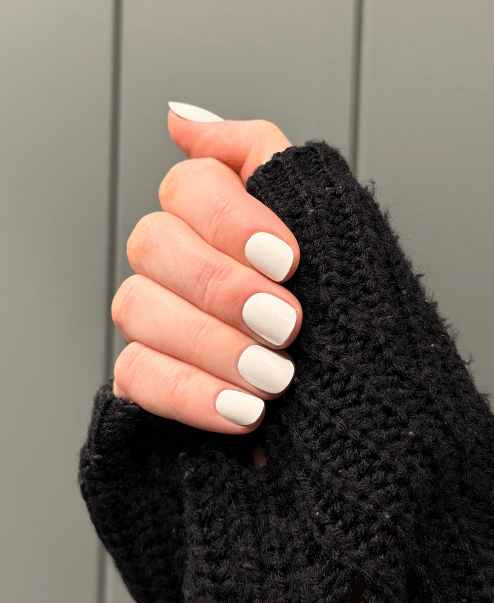 A hand wearing white press on nails with a black jumper