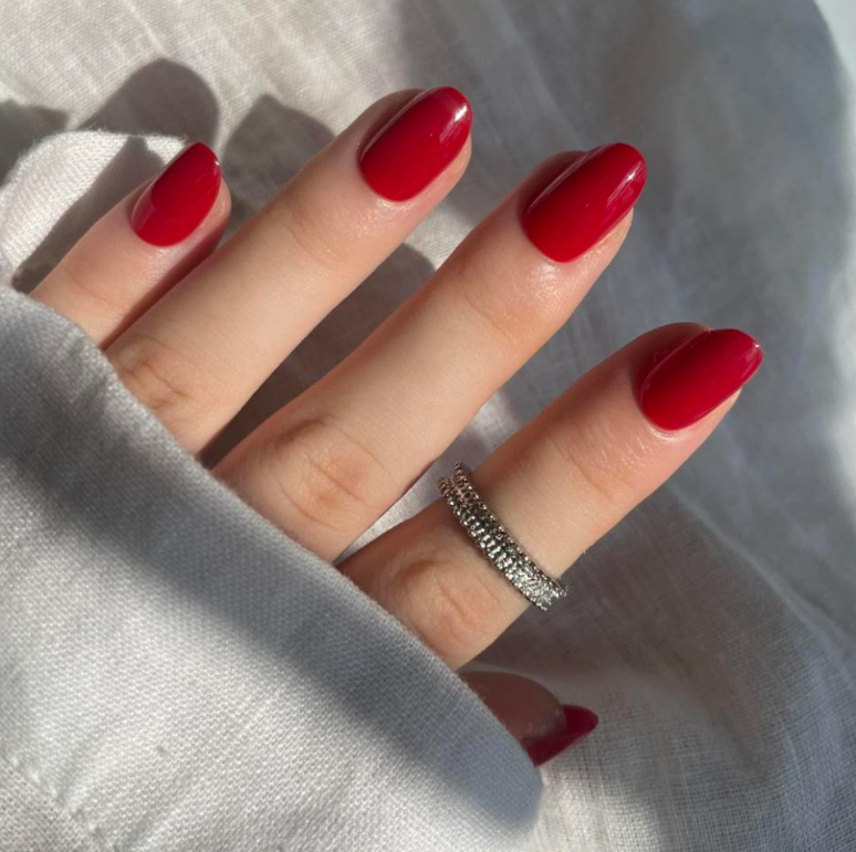 Hand with red nails and a silver ring on a light background