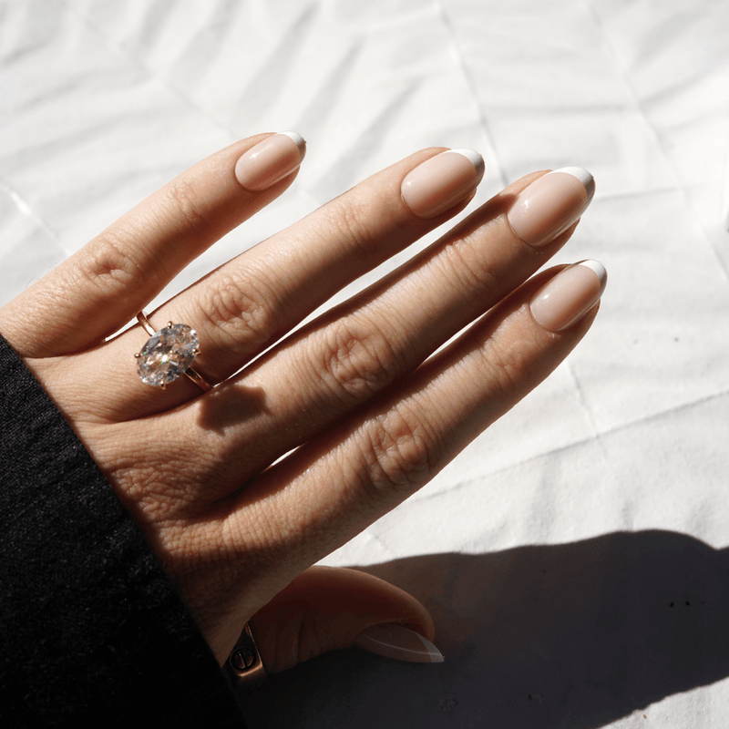 A close-up of a hand wearing a silver ring with a large clear rectangular gemstone, resting on a wooden table with a cocktail glass in the background.