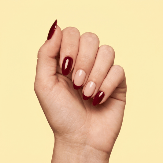 A close-up of a hand with manicured nails painted in a glossy deep burgundy color, set against a solid pale yellow background.