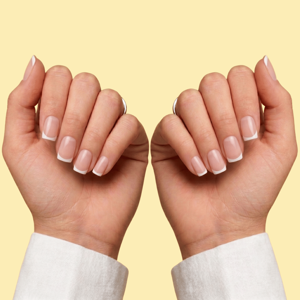 A close-up of two hands with neatly manicured French tip nails, shown against a solid pale yellow background.