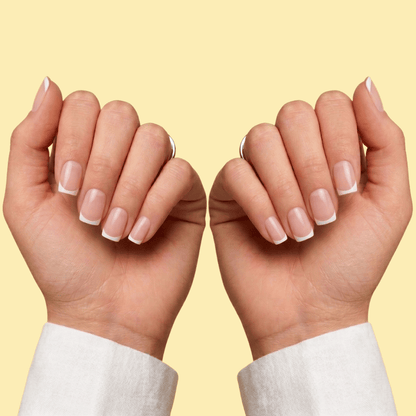 A close-up of two hands with neatly manicured French tip nails, shown against a solid pale yellow background.