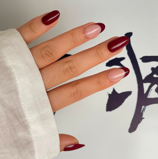 Hand with maroon and french nail polish against a light background