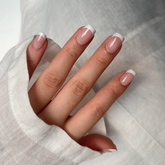 A hand with square french tip press on nails on a fabric background