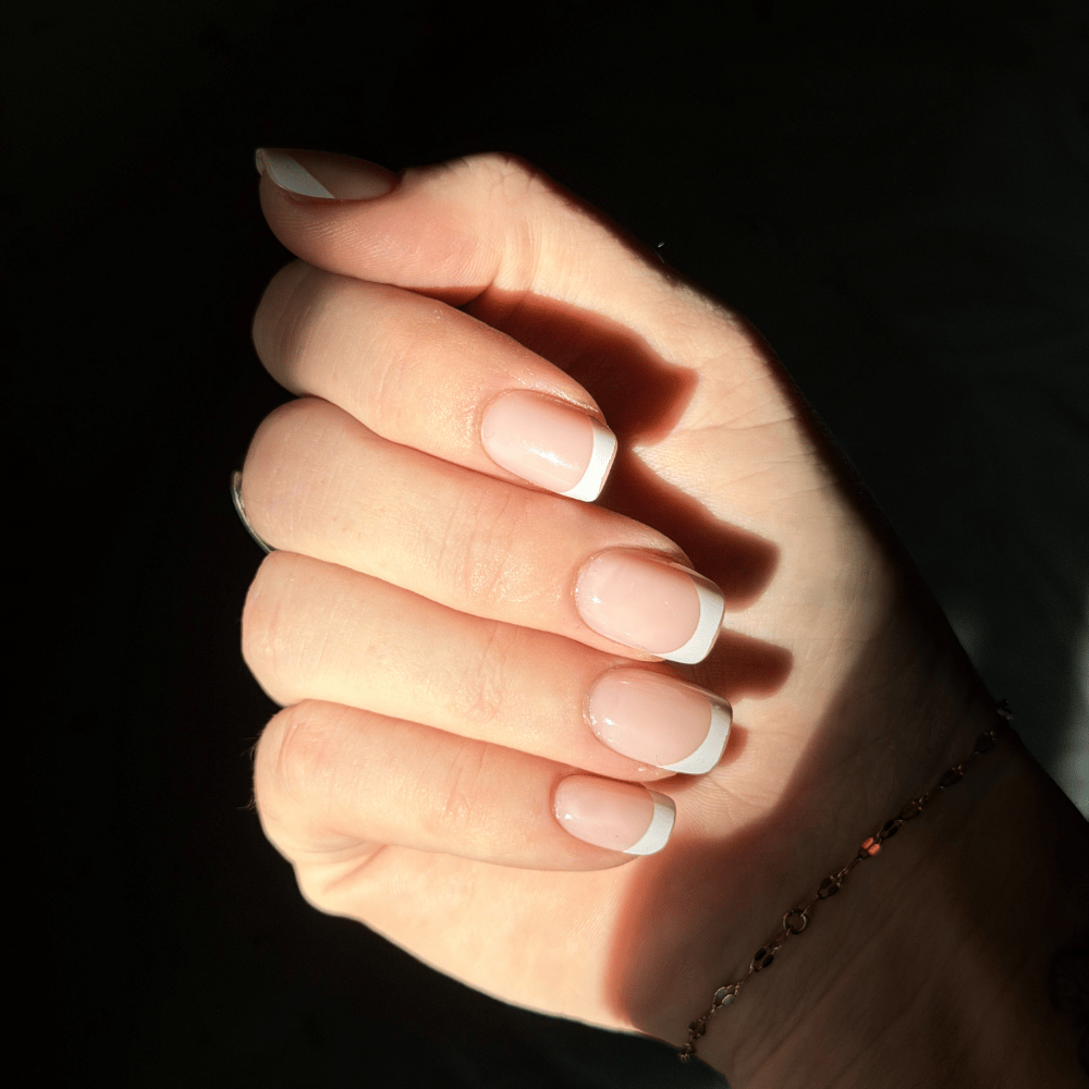 Close-up of a hand with white nail polish on a dark background