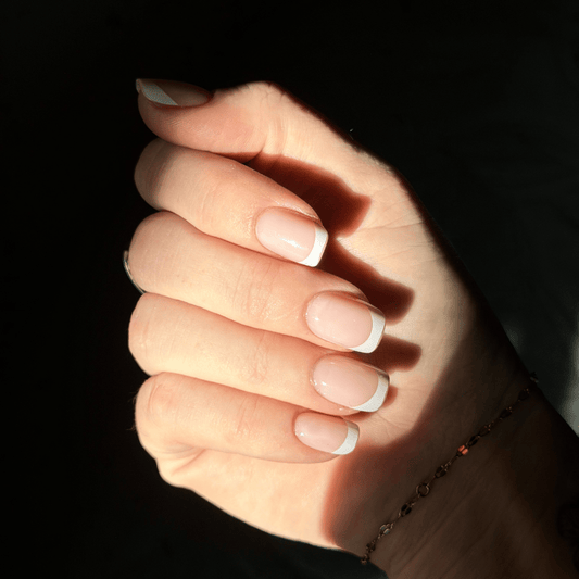 Close-up of a hand with white nail polish on a dark background