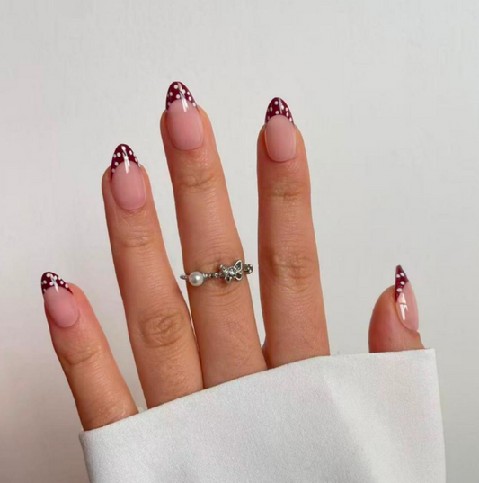 A hand with a silver ring wearing press on nails on a white background