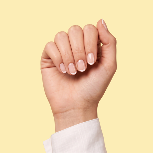 A close-up of a hand with a classic French manicure, showing a glossy pale pink base and crisp white tips, set against a solid pale yellow background.