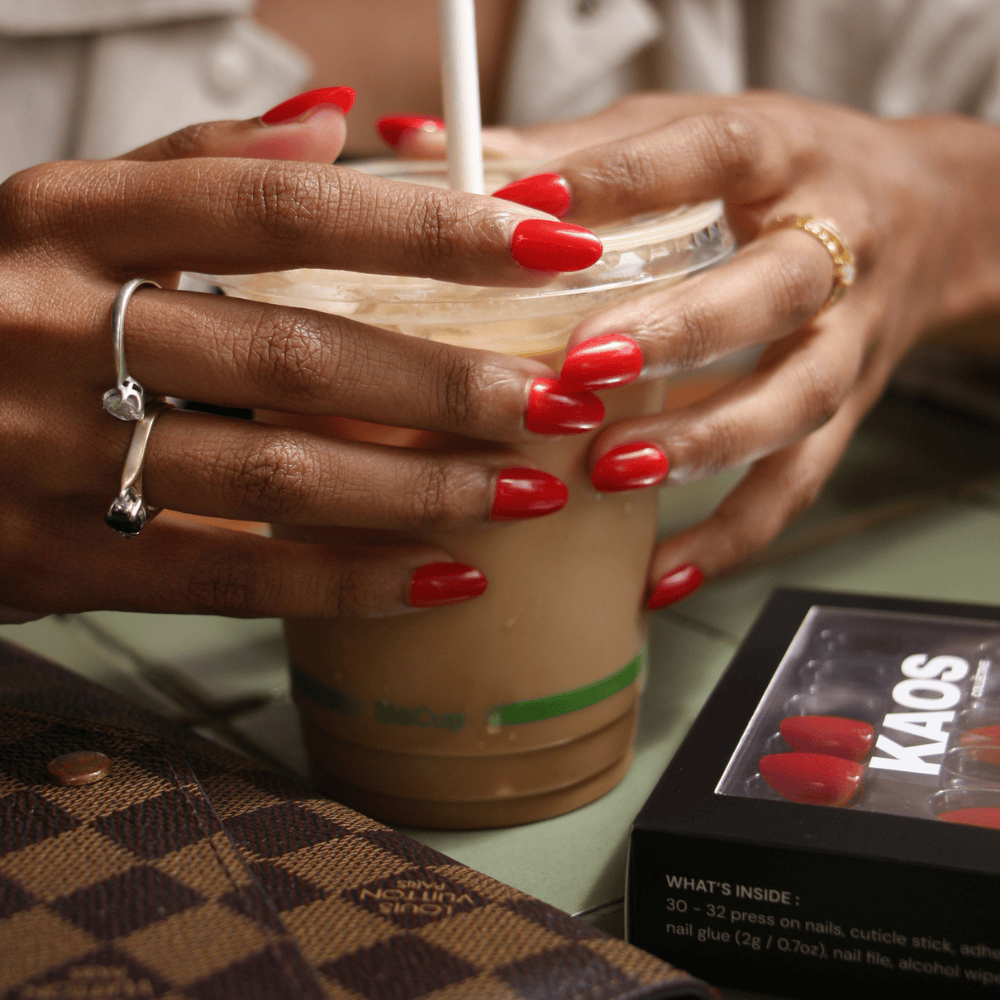 Person holding a Starbucks iced coffee with red nails, wearing rings.