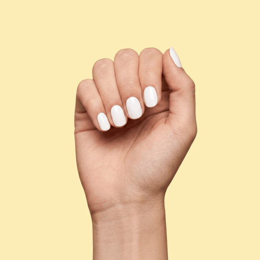 A close-up of a hand with neatly manicured, glossy white fingernails, posed against a solid pale yellow background.