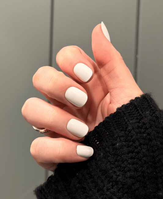 A hand wearing white press on nails with a black jumper