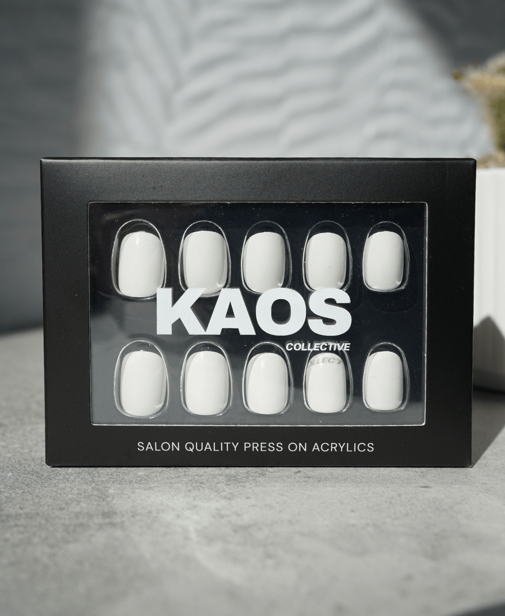 Box of white press-on nails with 'KAOS Collective' branding on a gray surface.