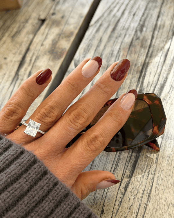 A close-up of a hand with a silver ring featuring a large clear rectangular gemstone, resting on a rustic wooden table next to tortoiseshell sunglasses.