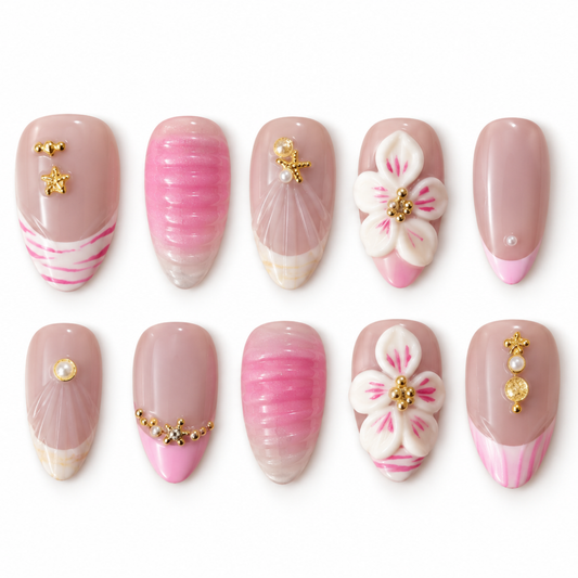 Ten false press-on nails arranged in two rows on a white background, featuring a soft nude pink base with various nail art designs including pink stripes, white cherry blossom flowers with gold details, pearl accents, and metallic gold charms.