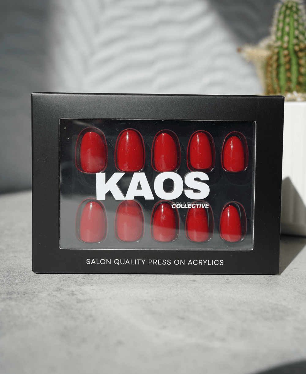 Box of red press-on acrylic nails with 'KAOS Collective' branding on a neutral background.